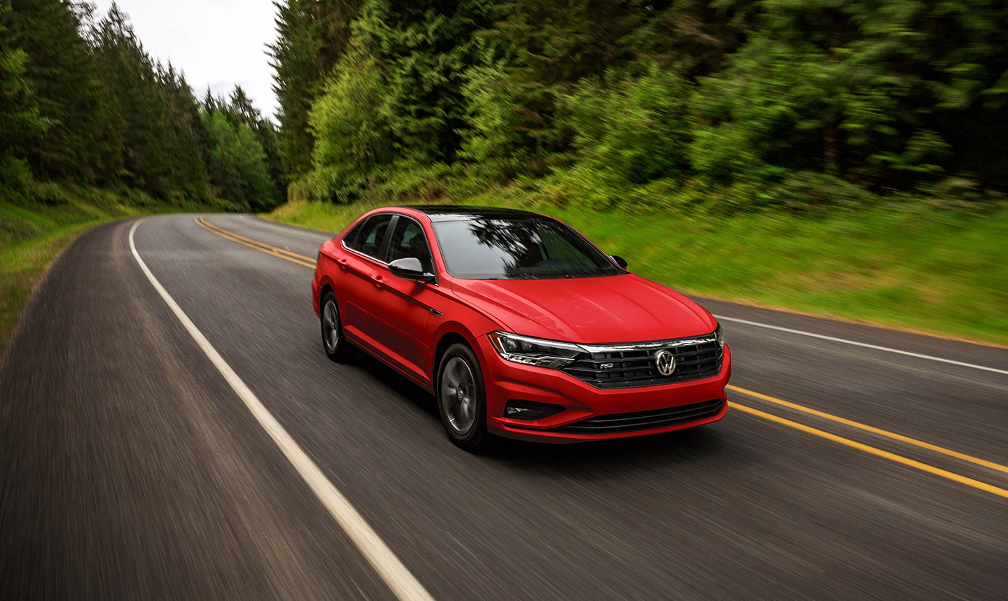 A red 2021 Volkswagen Jetta driving on a road with trees.